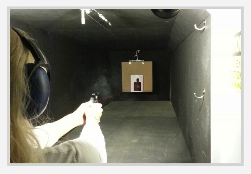 A shooter on the climate controlled indoor range firing at a paper target in a lit lane